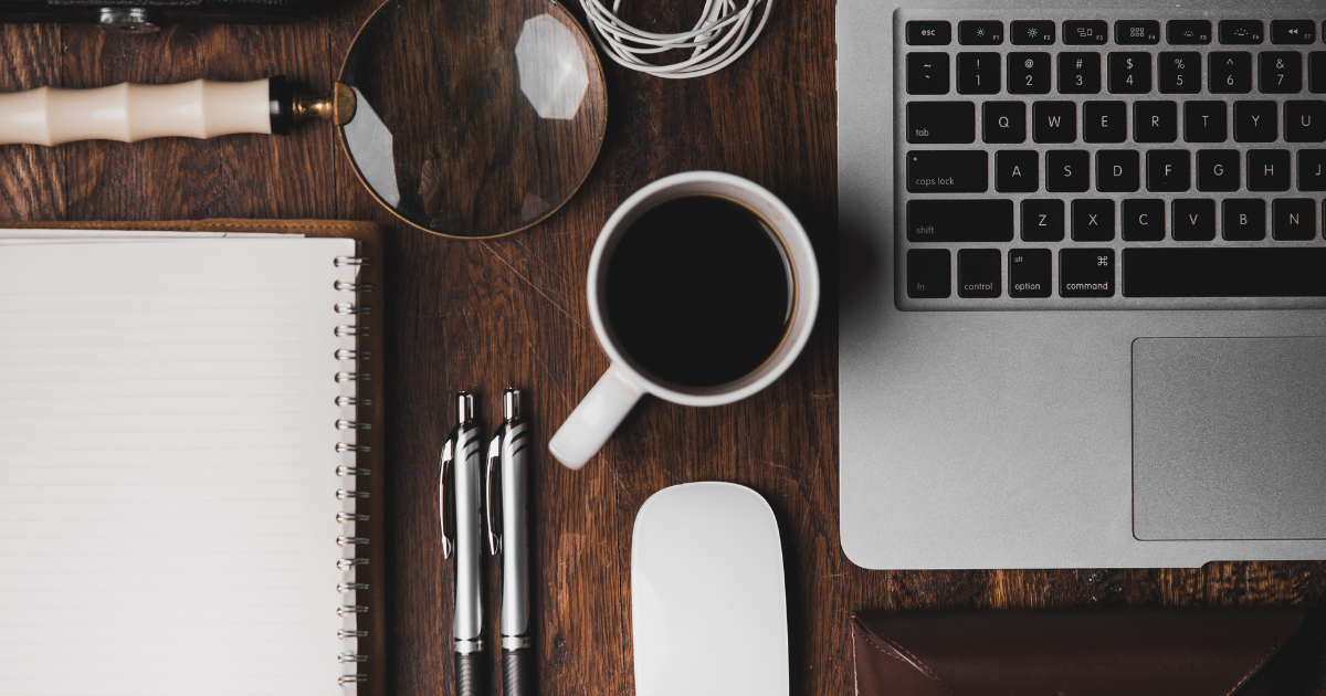 A desk top with a laptop, notebook, pen.